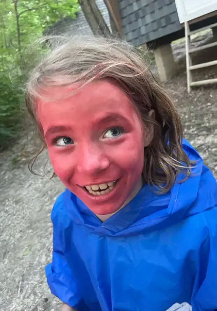 Girl camper laughing outdoors in a blue rain poncho