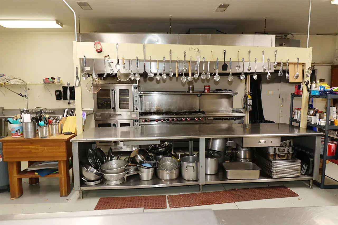 Commercial kitchen with stainless steel range, oven, and hanging utensils