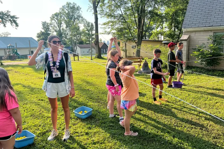 Campers and a counselor playing an outdoor string game with colored eggs and baskets